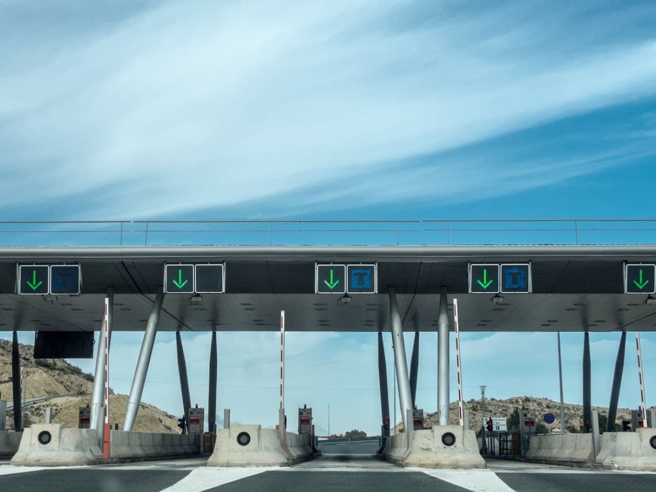 Open automated toll gates spanning a motorway, with green arrows over every lane.