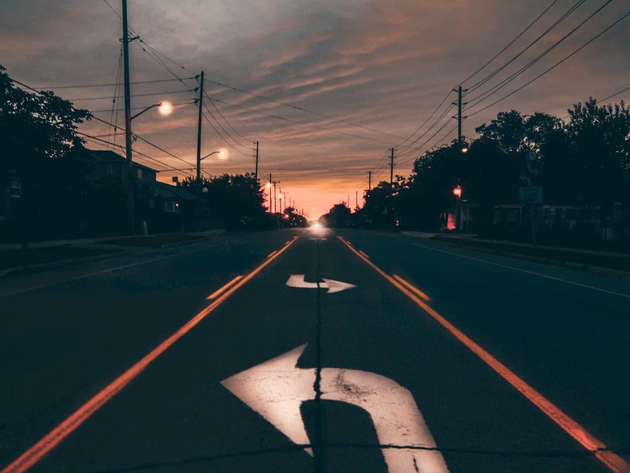 A road at dusk with a painted arrow that turns back on itself.
